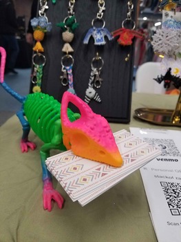 A rainbow chameleon skeleton made of plastic, holding a stack of cards in its mouth.